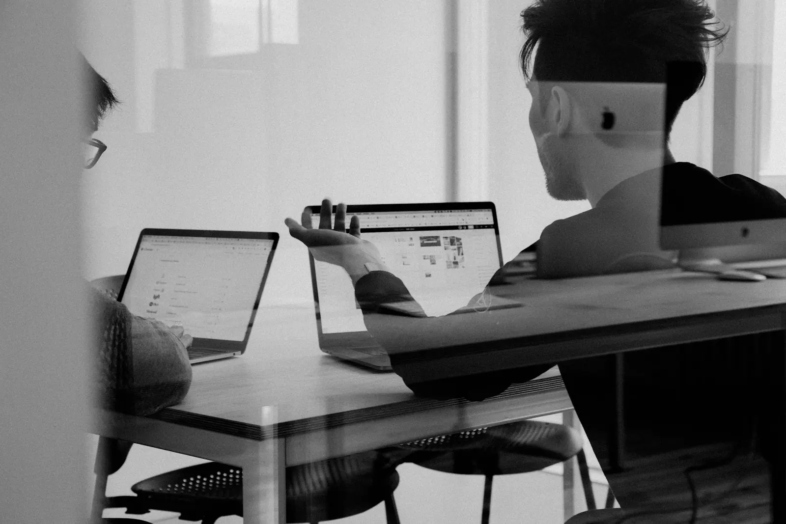 Two colleagues at a workstation, one using a desktop and one a phone