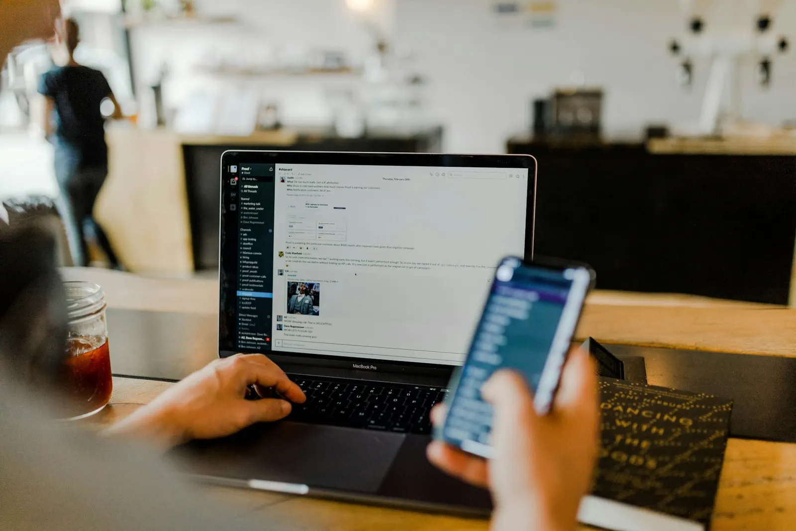 Person holding a phone while working on a laptop