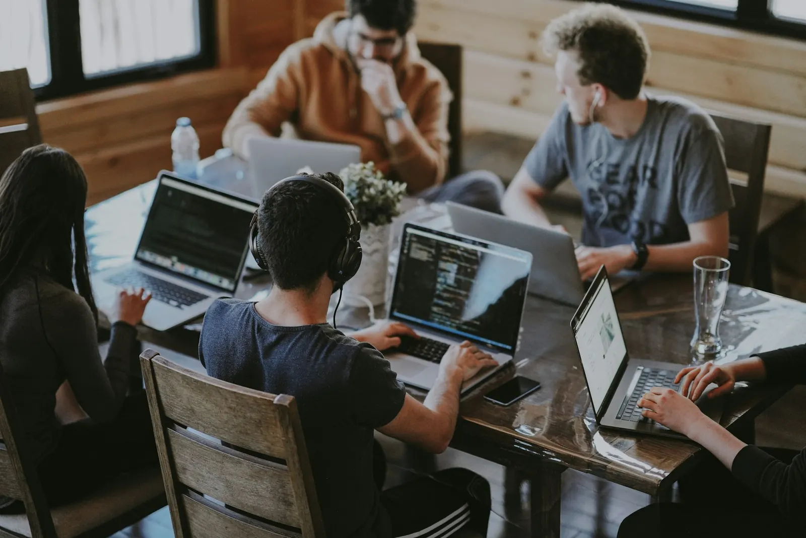 Three people collaborating around laptops at a wooden table
